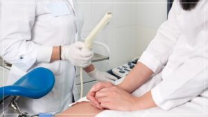 A medical professional in a white lab coat holding a transvaginal ultrasound probe, preparing for a gynecological exam, while a patient sits in an examination chair.